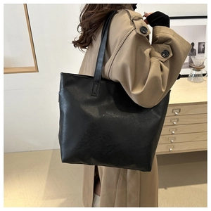 Side view of black large capacity tote bag worn by model in minimalist indoor setting