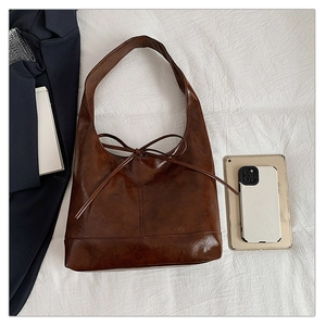Flat lay of a brown faux leather tote bag with bow detail next to a tablet and suit