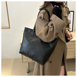 Minimalist black leather tote bag worn with a classic trench coat for a stylish look