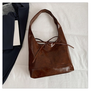 Detail of a dark brown glossy leather hobo bag featuring a decorative bow accent