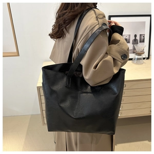Detailed view of a large black faux leather tote bag worn by a model in a minimal interior
