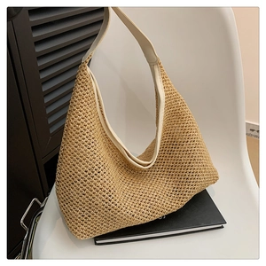 Detail of hand-woven straw tote bag featuring wide cream leather shoulder strap on a chair
