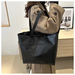 Modern black leather tote bag worn by a model in a minimalist indoor setting