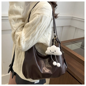 Detail of dark brown ruched crescent shoulder bag with a plush cloud pendant accessory