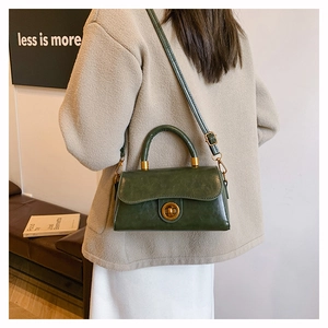 Detail of dark green retro small square bag with golden twist lock on a leather sofa