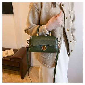 Detail of dark green vintage handbag showing gold metal lock and leather texture on model
