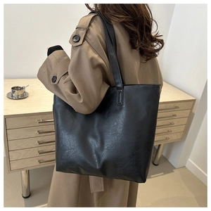 Close-up of a large black leather tote bag worn with a khaki trench coat in a cozy room
