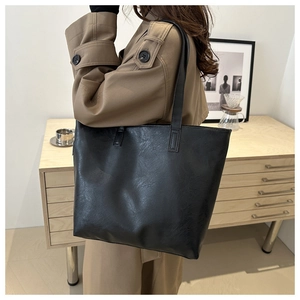 Detail view of large black tote bag with wrinkled leather texture on female model's shoulder