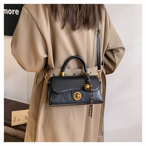 Detail view of black vintage leather satchel with golden clasp and decorative ball charm
