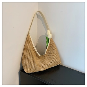 Detail view of a woven straw tote bag featuring creamy white leather straps and trim