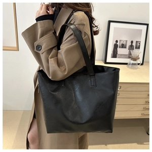 Side view of a large black minimalist tote bag shown on model in a modern room