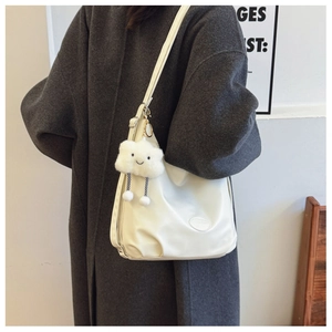 Close-up of white leather tote bag with smiling cloud charm on grey winter coat