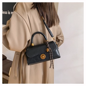 Close-up of black leather handbag with round metal twist lock and woven rope accessory