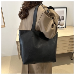 Close-up of minimalist black PU leather tote bag with wide shoulder straps worn by model