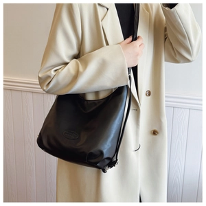 Minimalist black crescent shoulder bag shown on model with chic beige blazer attire