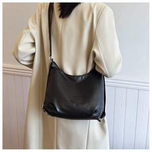 Detail view of black crescent leather shoulder bag worn over a cream trench coat