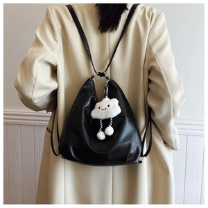 Close-up of a black soft leather backpack with a white plush cloud charm on a beige suit