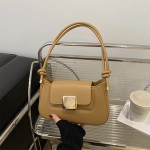 Minimalist camel leather baguette shoulder bag with gold buckle on a modern metal display