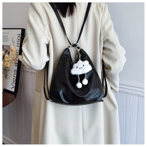 Detail of black leather tote bag with a white plush cloud charm on a beige trench coat