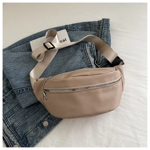 Close-up of beige leather belt bag with silver zipper on denim jacket background