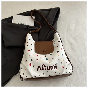 Dettaglio della borsa tote a pois colorati con tracolla in pelle su sfondo abito grigio