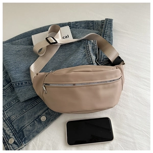 Top view of beige crossbody chest bag with silver zippers and nylon strap next to a phone