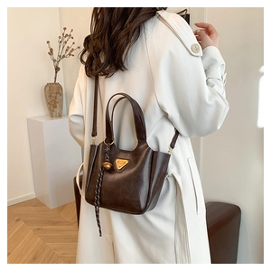 Detail of dark brown leather bucket bag with gold triangle logo and tassel pendant