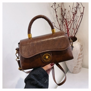Detail of vintage brown leather handbag featuring golden twist lock and round handle