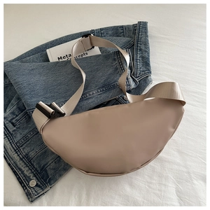 Detail of a milk coffee crescent crossbody bag with nylon strap on denim jacket background