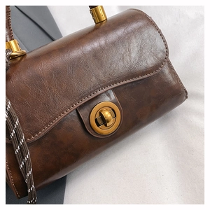 Detail of vintage brown leather handbag with gold circular twist lock and woven strap