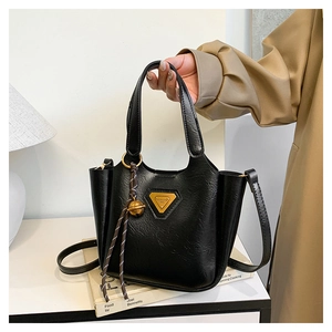 Detail of black faux leather bucket bag with gold triangle plaque and spherical charm