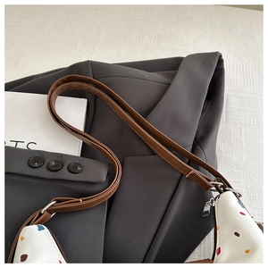 Dettaglio della borsa tote a pois con tracolla in pelle marrone su blazer grigio
