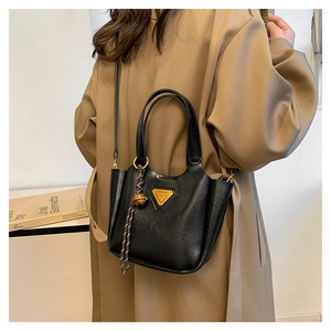 Detail of black vintage bucket bag with gold logo and woven charm on khaki trench coat