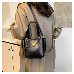 Detail of black glossy leather bucket bag with orange triangle logo and woven tassel