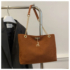 Detail of caramel suede tote bag with chain strap and gold deer pendant ornament