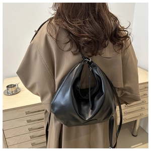 Detail view of a black glossy moon-shaped hobo bag styled in a casual city lifestyle setting