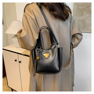 Detailed view of a black leather crossbody bag with gold logo and bell charm accessory