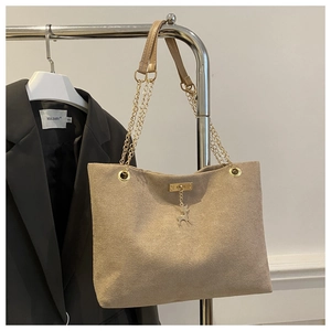 Detail of beige suede tote bag with golden elk pendant and chain handle displayed on a rack