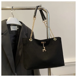 Detail of black suede tote bag featuring a gold chain strap and elegant deer pendant charm