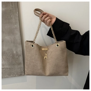 Detail of light brown suede tote bag featuring a gold deer charm and metal chain strap