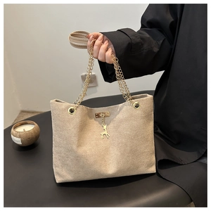 Detail of beige suede tote bag with elegant gold chain handle and deer-shaped pendant