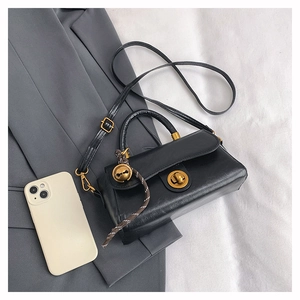 Detail of black leather handbag with gold twist lock and plaid charm on a gray blazer