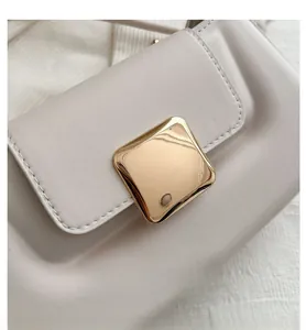 Détail d'un sac baguette blanc crème avec boucle en métal doré et coutures précises