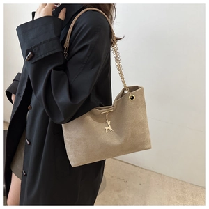 Detail of khaki suede tote bag featuring a gold chain strap and a small deer charm