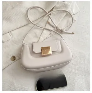 Détail du sac baguette crème avec boucle dorée et téléphone pour comparer la taille