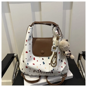 Dettaglio della borsa tote bianca a pois con patta in pelle marrone su sedia nera