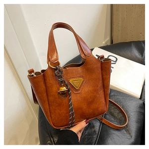 Detail of brown vintage tote bag with gold triangle logo and woven bell charm on leather sofa