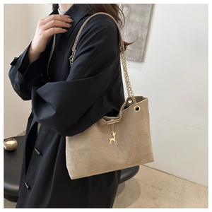 Khaki suede tote bag with golden deer pendant and chain strap shown on shoulder