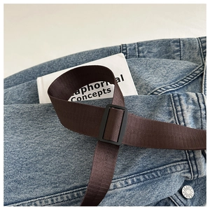 Detail of adjustable dark brown woven strap with durable black plastic buckle on jeans