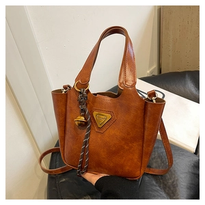 Detail of vintage brown leather tote bag with brass logo and woven bell charm accessory